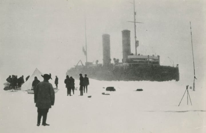 Старая фотография: во льдах стоит большой пароход с двумя трубами, на снегу люди и палатка